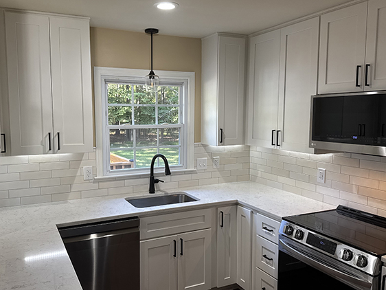 Modern kitchen with white cabinets, stainless steel appliances, and a window overlooking a backyard.